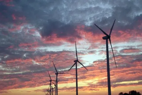 Wind turbines silhouetted against a colorful sunset sky.